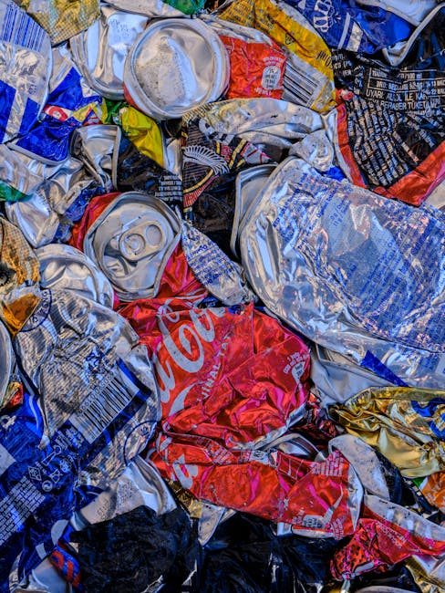 A row of outdoor rubbish bins positioned along a pavement adjacent to a brick wall, with the bins arranged in a line and each featuring different colored lids—green, red, and blue—indicating separ